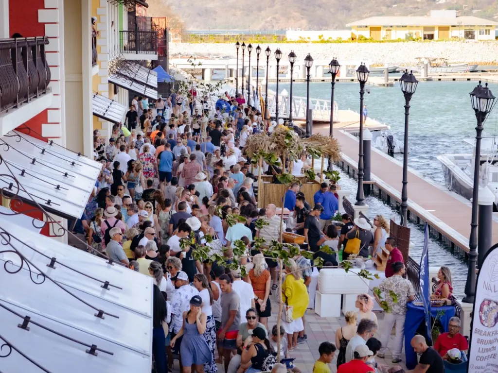 A crowd of people walking along a boardwalk near the water.